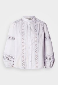 Balta blūze ar augstu apkakli, pogu aizdari un pūkainām piedurknēm. Iezīmējas sarežģītiem mežģīņu paneļiem ar apļveida rakstiem pa priekšpusi un piedurkņu malām.