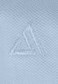 Lichtblauwe gebreide stof heeft een getextureerd driehoekig logo dat in een iets donkerdere tint is geborduurd. De steken zijn schoon en nauwkeurig.