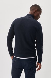 Pulover tricotat texturat de culoare bleumarin, cu un guler înalt și mâneci lungi, purtat peste pantaloni bleumarin, prezentat dintr-o perspectivă din spate.