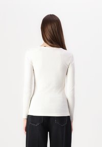 Hvid langærmet top med ribbet struktur, tætsiddende design og rund halsudskæring, parret med mørk denimbukser med nitter.