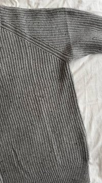 Gray knitted sweater featuring ribbed texture and a relaxed fit, with a wide neckline and long sleeves. The fabric appears soft and cozy.