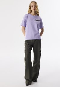 Lavendel katoen t-shirt met korte mouwen en zwarte tekst, gecombineerd met donkergroene hoge cargo broek met zijzakken.