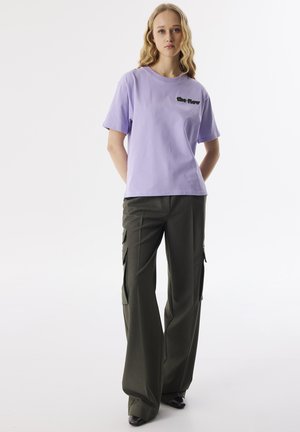 Lavender cotton t-shirt with short sleeves and black text, paired with dark green high-waisted cargo pants featuring side pockets.
