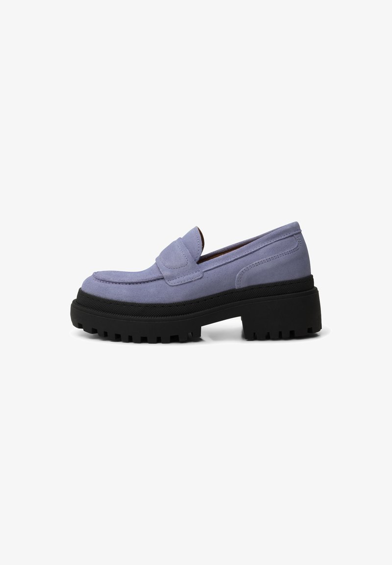 Zapato tipo mocasín de gamuza de color morado claro con suela de goma negra gruesa y con textura antideslizante. Presenta una correa decorativa a lo largo del empeine.