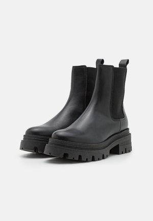 Mustad mustad, musta nahast pahkluu saapad elastsete küljepaneelidega, paks kummine tall, ja plokiahjas disain. Omab tõmblukke lihtsaks selga panemiseks.