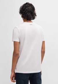 Hvid bomulds T-shirt med korte ærmer, rund hals og et lille "HUGO" logo på den bagerste hals. Glat tekstur og standard pasform.