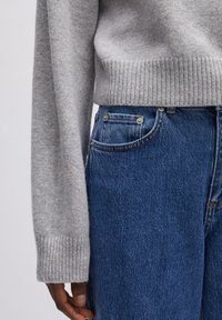 Grijze gebreide trui met geribde onderkant en manchetten, gecombineerd met blauwe denim jeans met contrasterende stiksels en vo pockets.
