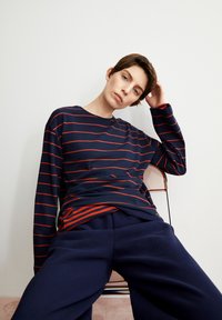 Dunkelblaues Langarmshirt mit roten horizontale Streifen, kombiniert mit weiten dunkelblauen Hose. Glatter Stoff mit lässiger Passform.