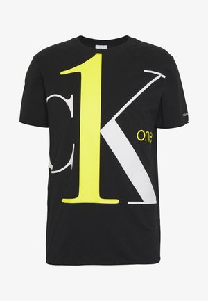 Schwarzes T-Shirt mit kurzen Ärmeln, großer gelber Zahl "1" und übergroßen weißen und grauen Buchstaben "K", kleinem gelbem Schriftzug "one", Calvin Klein Logo auf dem Ärmel.