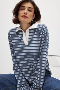 Polo a maniche lunghe a righe blu e bianche. Presenta un colletto e una vestibilità rilassata. Il materiale è morbido con dettagli di cucitura visibili.