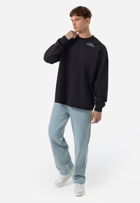 Black oversized sweatshirt with long sleeves and crew neck, featuring small blue text detail; paired with light blue jeans and white sneakers.