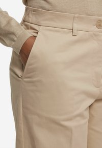 Beige bomullsmixbyxor med en mjuk yta, som har en framficka, en sydd midja och en enkel knappstängning.