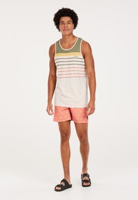 Heren tanktop in lichtbeige met groene, gele en roze strepen; gecombineerd met roze shorts met witte palmbomenpatronen; zwarte sandalen.