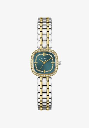 Kaksivärinen hopea- ja kultametallirannekello, jossa on vihreä neliönmuotoinen kellotaulu, kristallimerkinnät, kullanväriset osoittimet ja "GUESS"-logo kellotaulussa.