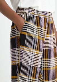 Flerfärgade rutiga byxor med en kombination av svart, vitt, lila och guld, med ett elastiskt midjeband och sidofickor.