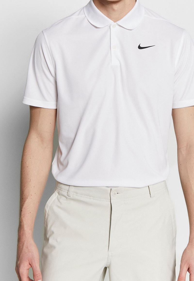 Bílá polo košile vyrobená z prodyšného materiálu, s klasickým límcem, krátkými rukávy a malým černým logem Nike na hrudi.