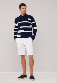 Maglione navy con motivo a strisce astratte bianche, abbinato a pantaloni corti bianchi e espadrillas navy. Tessuto morbido, vestibilità rilassata e scollatura semplice.