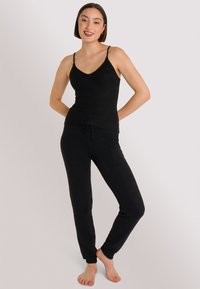 Top in maglia nera con spalline sottili abbinato a pantaloni della tuta neri a gamba affusolata con vita regolabile e polsini a costine. Texture liscia.
