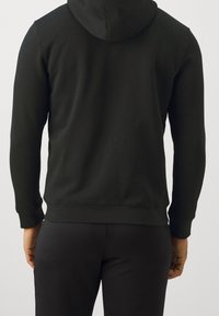 Sweatshirt à capuche noire en tissu doux, avec des manches longues, une poche kangourou et une ceinture ajustée. Design simple, sans motifs.