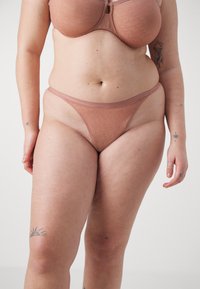Biustonosz i stringi wykonane z miękkiego, cielistego materiału z subtelnym wzorem geometrycznym. Cienkie ramiączka i bezszwowe krawędzie definiują design.
