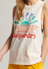 Biały bezrękawnik z bawełny z kolorową grafiką słońca i fal oraz napisem "Superdry" w wyraźnej czerwieni. Miękka tekstura, luźny krój.