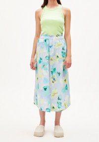 Vaatetus pitkä maksihame, jossa on vaaleansininen perusteksti ja vihreitä sekä keltaisia kuvioita, yhdistettynä ilmanhihaisella vihreällä paidalla ja vaaleanbeigeillä klompilla.