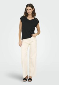 Czarny top z dekoltem w serek z koronkowymi akcentami na ramionach, w połączeniu z jasnobeżowymi spodniami o szerokich nogawkach i czarnymi klapkami w kwiaty. Gładki materiał, luźny krój.