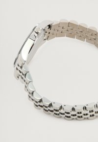 Ceas din oțel inoxidabil argintiu cu carcasă rectangulară, bezel texturat și brățară cu linkuri intercalate în formă de semilună și linkuri plate.