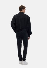 Chaqueta de mezclilla negra con un corte holgado, combinada con jeans negros ajustados y zapatillas blancas, vista desde atrás, resaltando la textura y la forma.