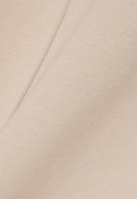 Zacht beige stof met een fijne weving, met een close-up van een rechte naad en zachte plooien.