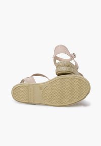 Sandali beige con design a cinturino e tacco in espadrille intrecciato. La suola in gomma testurizzata presenta un motivo a zigzag. Dettaglio della chiusura a fibbia visibile.