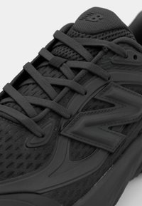 Black athletic shoe featuring a mesh upper, rubber accents, textured materials, and prominent branding on the side.