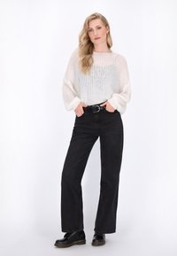 Leichter, gestrickter cremefarbener Pullover mit weiten Ärmeln, kombiniert mit hochgeschnittenen schwarzen Jeans und schwarzen Schnürstiefeln, die eine glatte Textur aufweisen.