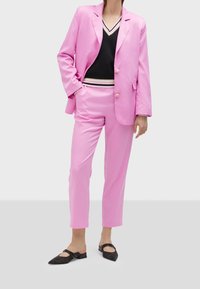 Rosa blazer och matchande byxor i mjuk tyg; svart linne med flerfärgade ränder; texturerade svarta ballerina med spetsig tå.