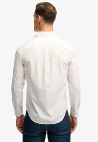 Witte blouse met lange mouwen, voorzien van een standaardkraag en knoopmanchetten, gemaakt van gladde stof met een getailleerde pasvorm en een afgeronde zoom.