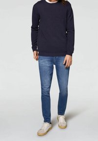 Pullover in maglia color navy, maniche lunghe, collo rotondo; abbinato a jeans slim-fit azzurri e sneakers beige con suole bianche.
