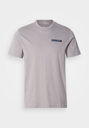 T-shirt en coton gris clair avec des manches courtes et un col rond. Présente un logo "CALVIN KLEIN" bleu marine sur la partie gauche de la poitrine. Design simple, texture lisse.