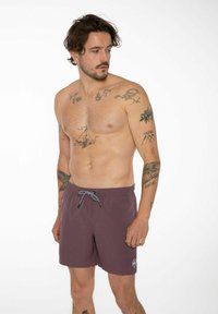 Pantaloni da bagno viola con tessuto testurizzato, vita elastica e coulisse bianca e nera. Include un piccolo logo sulla gamba inferiore.