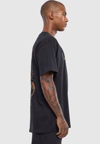 Sort bomulds T-shirt med korte ærmer, der har et grafisk design på ryggen. Lige snit, blød tekstur og en afslappet silhuet.