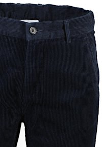 Marinblå kordfløyelsbyxor med vertikalt ribbad struktur, med knäppning och bältesöglor. Närbild som betonar tygdetaljer.