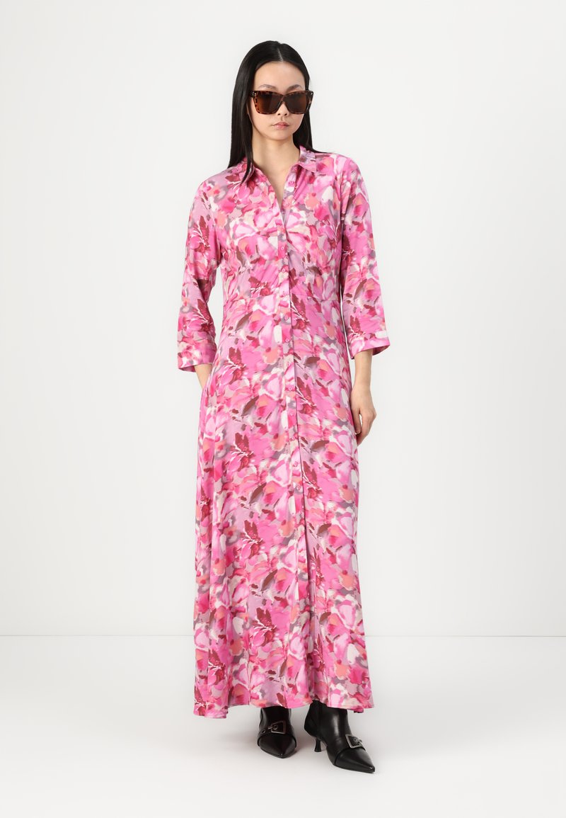 Długa, różowa sukienka w kwiaty z rękawami trzyczwartowymi i zapięciem na guziki z przodu. Wykonana z lekkiego materiału o gładkiej fakturze. Para ciemnych okularów przeciwsłonecznych.
