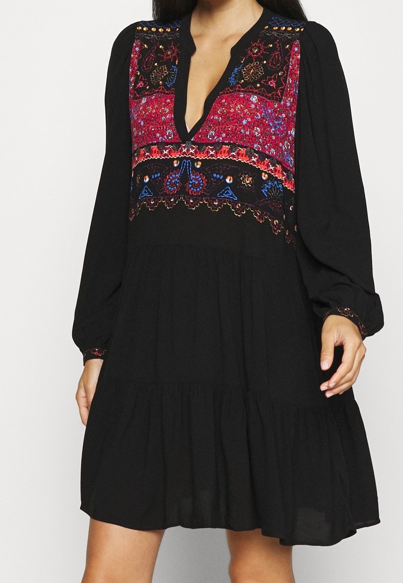 Robe noire à manches longues avec un col en V et des motifs brodés rouges, bleus et orange sur la poitrine et les poignets.