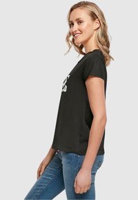 Sort bomulds t-shirt med korte ærmer, der har et hvidt tekstdesign, afslappet pasform og rund halsudskæring. Bæres med blå jeans.