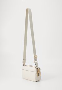 Crossbody bag in cream faux leather with a textured finish, two zip compartments, adjustable fabric strap, and gold-toned hardware accents.