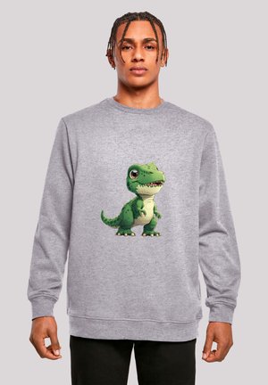 Young man with braided hair wears a grey sweatshirt featuring a green cartoon dinosaur with big eyes and small arms.