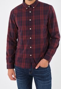 Rot und marineblaue karierte Button-Down-Bluse mit langen Ärmeln, Taschendetails und weißen Knöpfen. Kombiniert mit blauen Jeans.