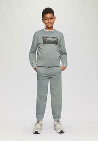 Conjunto de sudadera y pantalones de chándal a juego en gris, que presenta un gráfico impreso en el frente. Textura suave con puños acanalados y bolsillos laterales.