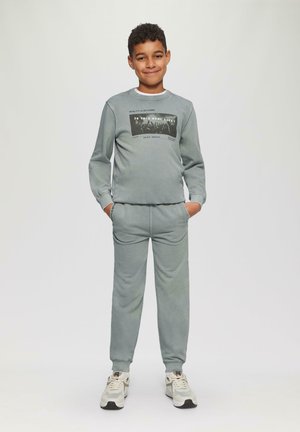 Grijze bijpassende sweatshirt en sweatpants set, met een geprinte grafische afbeelding op de voorkant. Zachte textuur met ribgebreide manchetten en zijzakken.