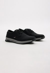 Zapatos negros con cordones fabricados en material sintético texturizado. Presentan suelas grises y un acento a rayas en contraste cerca del talón.