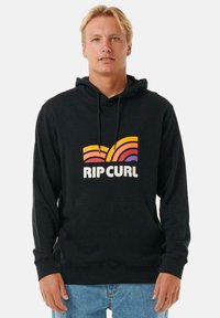 Sudadera negra con bolsillo canguro, que presenta un gráfico de olas retro colorido y el texto "RIP CURL". El material parece suave y texturizado.